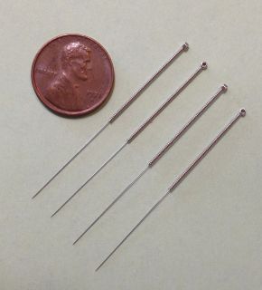 Four fine stainless steel acupuncture needles lying beside a one-cent coin
