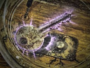 A metal key lying in a shallow glass dish, outlined by thin violet sparks of electrical discharge