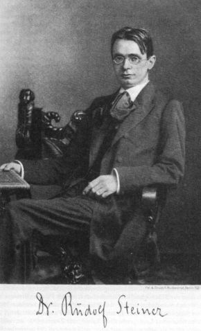 Black and white studio photograph of Rudolf Steiner seated in a carved chair, with his signature printed below
