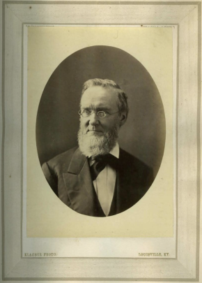 Oval portrait photograph of an older man with a white beard and round glasses, wearing a dark suit and bow tie