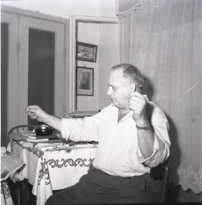 Black-and-white photograph of a seated man in a white shirt gesturing with both hands