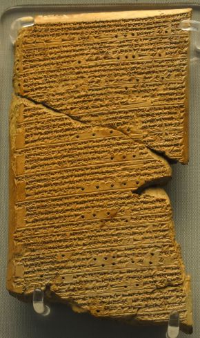 Broken clay tablet covered in rows of cuneiform writing, displayed upright on museum stands