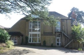 A two-storey pebble-dashed building with tall windows and an outside staircase, under a large cedar tree