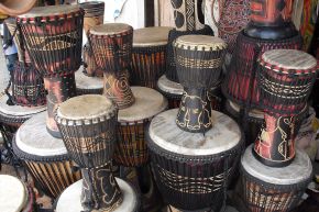 Rows of carved wooden djembe drums with pale skin heads and rope tuning