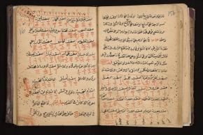An open handwritten Arabic book with lines of black and red script, and groups of short red strokes and dots arranged in rows inside drawn compartments